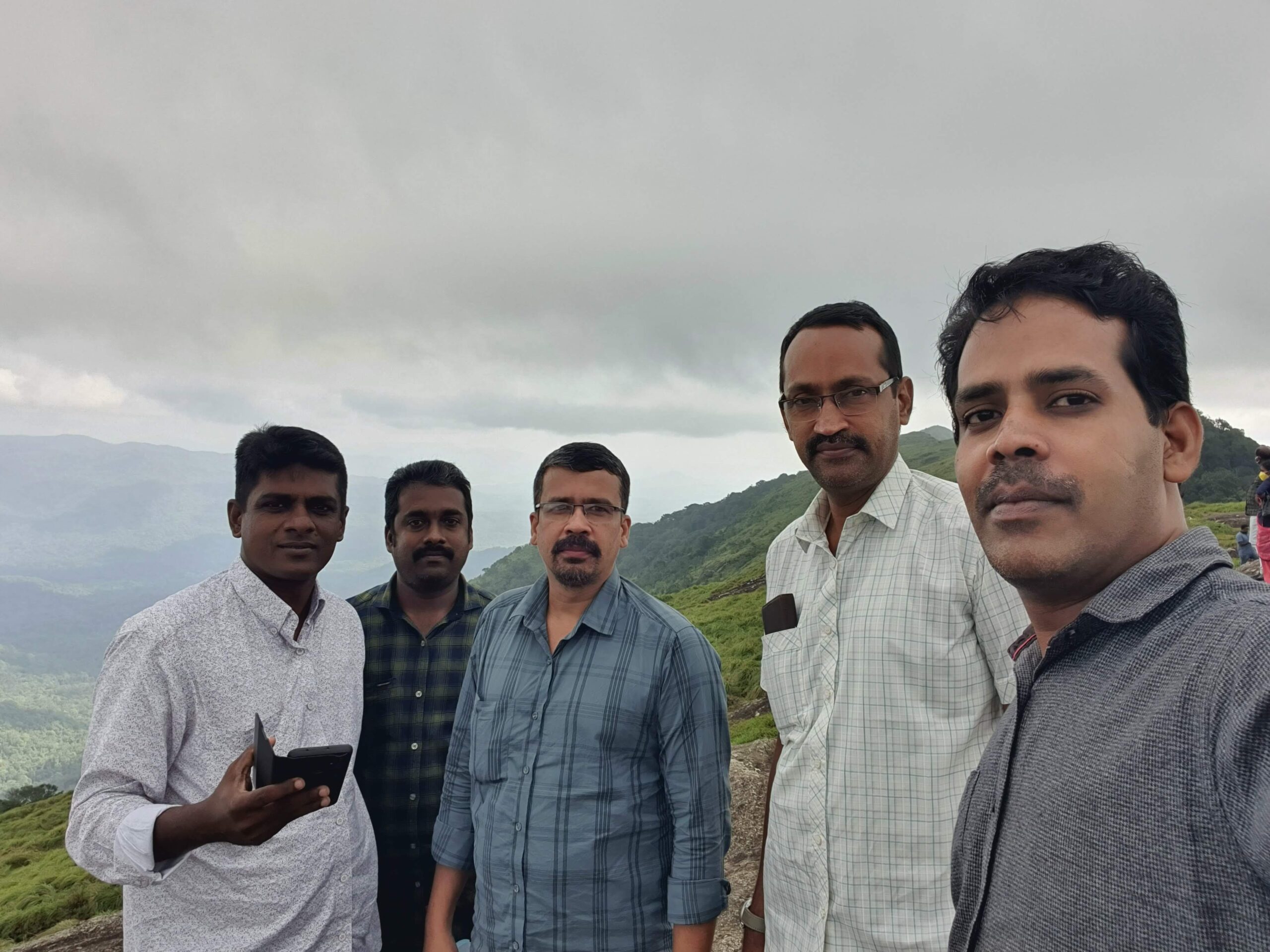 Friends sitting together on rocks, smiling and enjoying tea with misty hills in the background